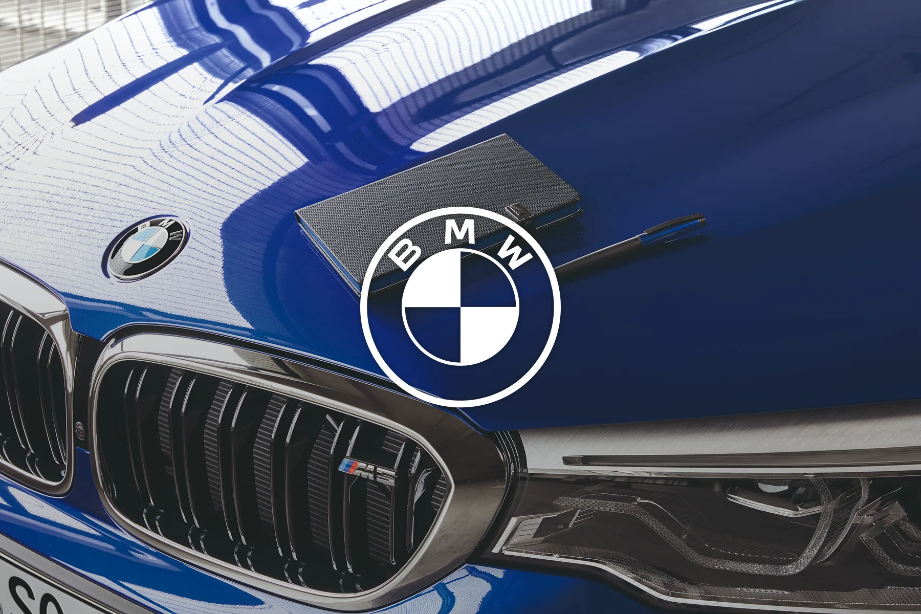 Notebook and pen sitting on the hood of a blue BMW